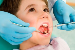 Un dentista explora la boca de un niño valiéndose de un espejo dental.